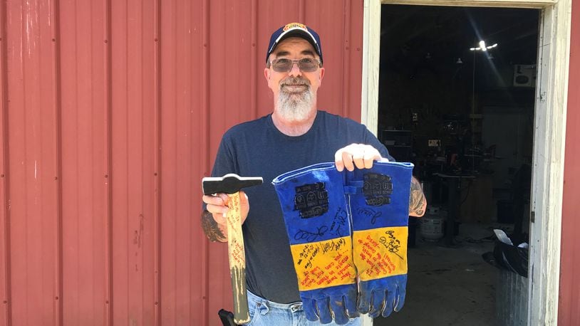 Bill Pyles stands outside of his forging workshop with the hammer and gloves he used on the show. His wife and children signed the hammer and gloves with encouraging messages. ALICE MOMANY/STAFF