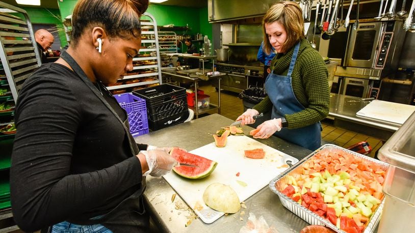 Volunteers Kris’Shawn Fleming, left, and Lisa Henderson cut fruit at House of Bread non-profit community kitchen Friday, Dec. 20, 2019 in Dayton. Fleming is volunteering while she is home from college for the holiday break. NICK GRAHAM/STAFF