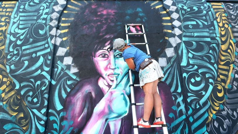 Tiffany Clark, founder of the Mural Machine, is creating a new mural at the entrance of the Oregon District in Dayton. The mural, created with brush and spray paint in 20 colors, depicts a woman at the center.  LISA POWELL / STAFF