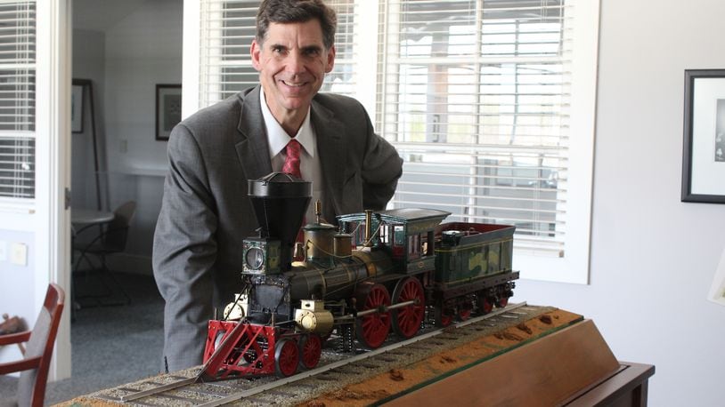 Brady Kress, president and CEO of Dayton History, displays a mini replica of the "Cincinnati," the first locomotive to pull a passenger train into Dayton. Carillon Historical Park is acquiring a full-sized replica of the train that will travel along a one-mile track that visitors can ride. CORNELIUS FROLIK / STAFF