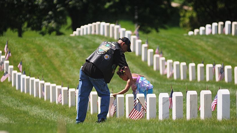 Army retired major Gary S. Conley gets help from his granddaughter, Kailynne Conley, 4, straightening flags at the Dayton National Cemetery on Memorial Day, May 30, 2016.