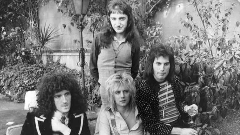 September 1976:  British rock group Queen at Les Ambassadeurs, where they were presented with silver, gold and platinum discs for sales in excess of one million of their hit single 'Bohemian Rhapsody', which was No 1 for 9 weeks. The band are, from left to right; Brian May, John Deacon (standing), Roger Taylor and Freddie Mercury (Frederick Bulsara, 1946 - 1991).  (Photo by Ian Tyas/Keystone/Getty Images)