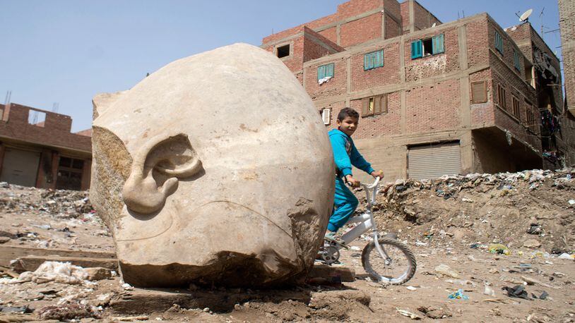 A boy rides his his bicycle past a recently discovered statue in a Cairo slum that may be of pharaoh Ramses II, in Cairo, Egypt, Friday, March 10, 2017. Archeologists in Egypt have discovered a massive statue that may be of pharaoh Ramses II, one of the country's most famous ancient rulers. The colossus, whose head was pulled from mud and groundwater by a bulldozer on Thursday, is around eight meters (yards) tall and was discovered by a German-Egyptian team.