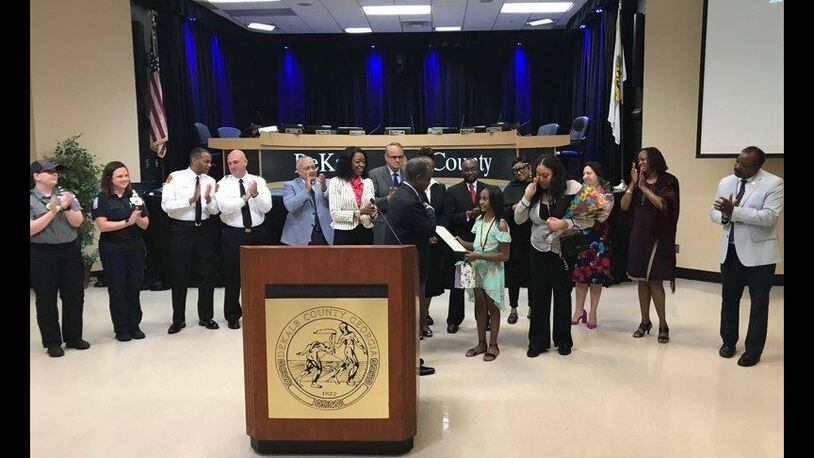 DeKalb County CEO Michael Thurmond presents a proclamation to Jayla Dallis, a 10-year-old girl credited with saving her sister from a near-drowning. Her mom Daneshia Dallis dabs away tears as officials applaud.