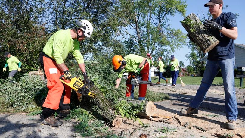 Members of the Southbrook Christian Church Disaster Response Team clear trees from a home on Fieldcrest Drive in Beavercreek last week as the July 28 deadline for free city curbside pickup of tree debris approached.  TY GREENLEES / STAFF