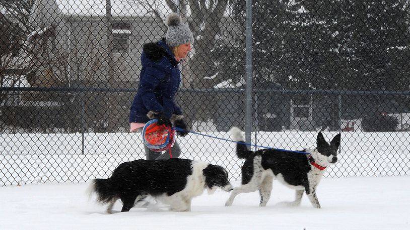 A woman walks her dogs near Shawnee Park in Xenia, on a snowy Wednesday, Feb. 10, 2021. Cold temperatures are expected this weekend, meaning recent snowfall will remain on the ground for an extended period of time. MARSHALL GORBY\STAFF