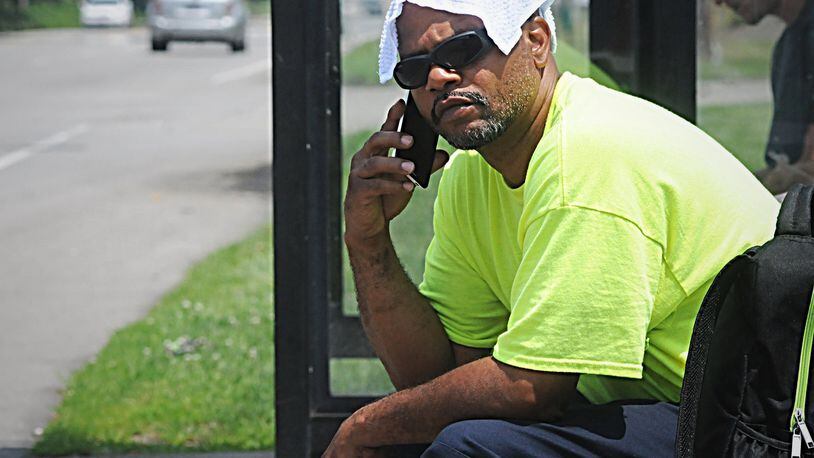 Yhanteg Marzette uses a wet wash cloth on his head keep cool while waiting for the bus on Springboro Pike Monday. Staff Photo Marshall Gorby
