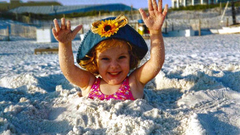 Three year old Caleigh Hildebrandt has some fun buried in the sand on the beach in Destin, Florida. The photo is now etched in granite and appears on the back on her grave memorial. CONTRIBUTED