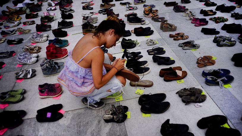 A woman places one of the hundreds of shoes in memory of those killed by Hurricane Maria in front of the Puerto Rico Capitol, in San Juan, Friday, June 1, 2018.  Puerto Rico's Institute of Statistics announced that it has sued the U.S. territory's health department and demographic registry seeking to obtain data on the number of deaths following Hurricane Maria as a growing number of critics accuse the government of lacking transparency.