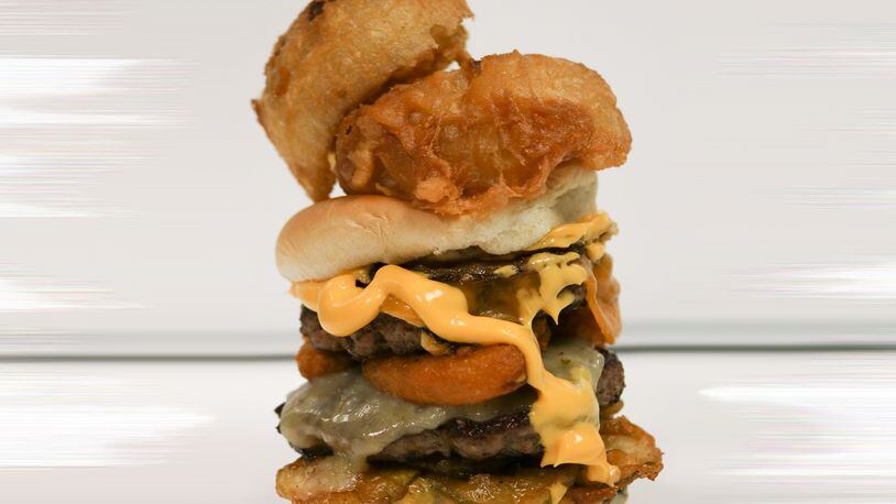 A Monroe flea market is offering prizes to the person who eats this colossal cheeseburger, stacked high with: three patties (equating to one whole pound of ground beef); slices of Pepper jack, American and Cheddar cheeses; mac and cheese bites; fried pickle slices; fried onions; and nacho cheese sauce all sandwiched between a large hamburger bun that’s then topped with two giant fried onion rings. CONTRIBUTED