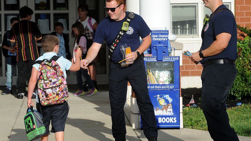 Miami Valley Fire District firefighter/Paramedics, from left,  Jerrod Widener and Caleb Young greet students with a new pencil at Jane Chance Elementary in Miamisburg, on the first day of school, Tuesday, Aug. 15, 2023. MARSHALL GORBY\STAFF