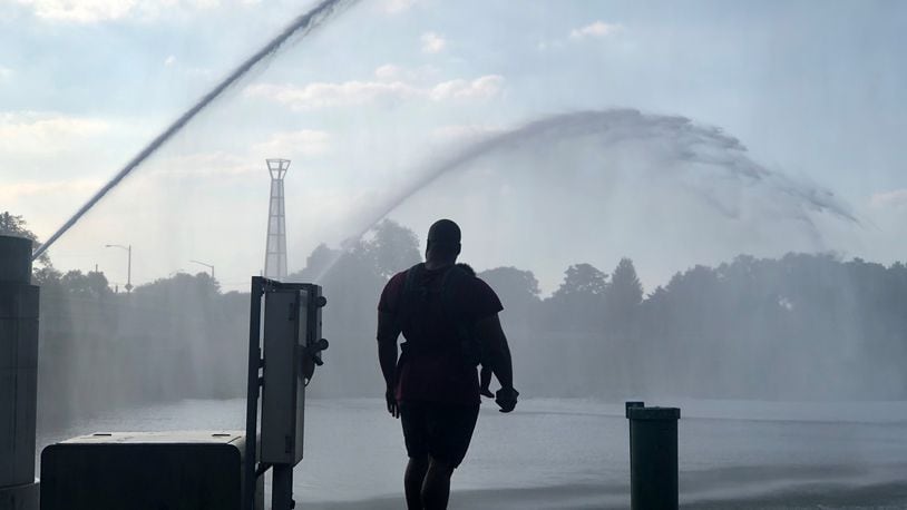 A man with a baby in a carrier watches the fountains in the river at RiverScape in the summer of 2020. CORNELIUS FROLIK / STAFF
