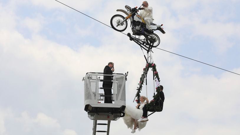 Pastor Stefan Gierung, left, stands in a cage atop of a fire service ladder in front of bride Nicole Backhaus, center, and groom Jens Knorr, right, both sitting in a swing dangling under a motorcycle with artist Falko Traber, top, during the wedding ceremony atop a tightrope in Stassfurt, Germany, Saturday, June 16, 2018.