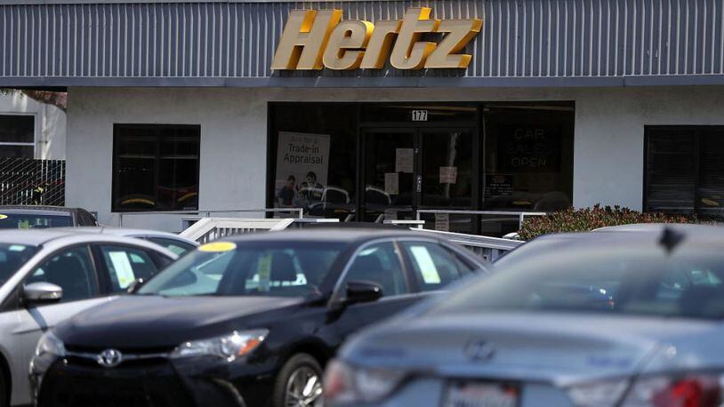 A sign is posted in front of a Hertz sales and rental car office.