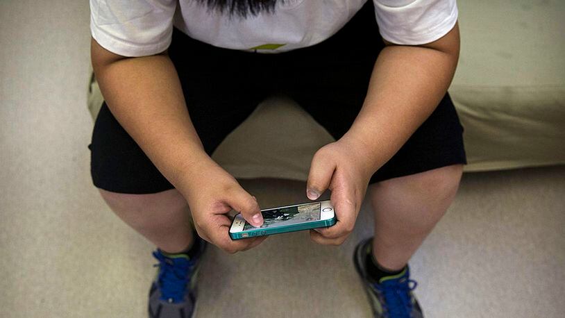 An overweight student plays a game on his mobile phone as he waits for a medical check before training at a camp held for overweight children on July 14, 2014 in Beijing, China.